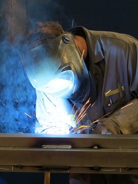 Machine operator working on a welding project while smoke arises.
